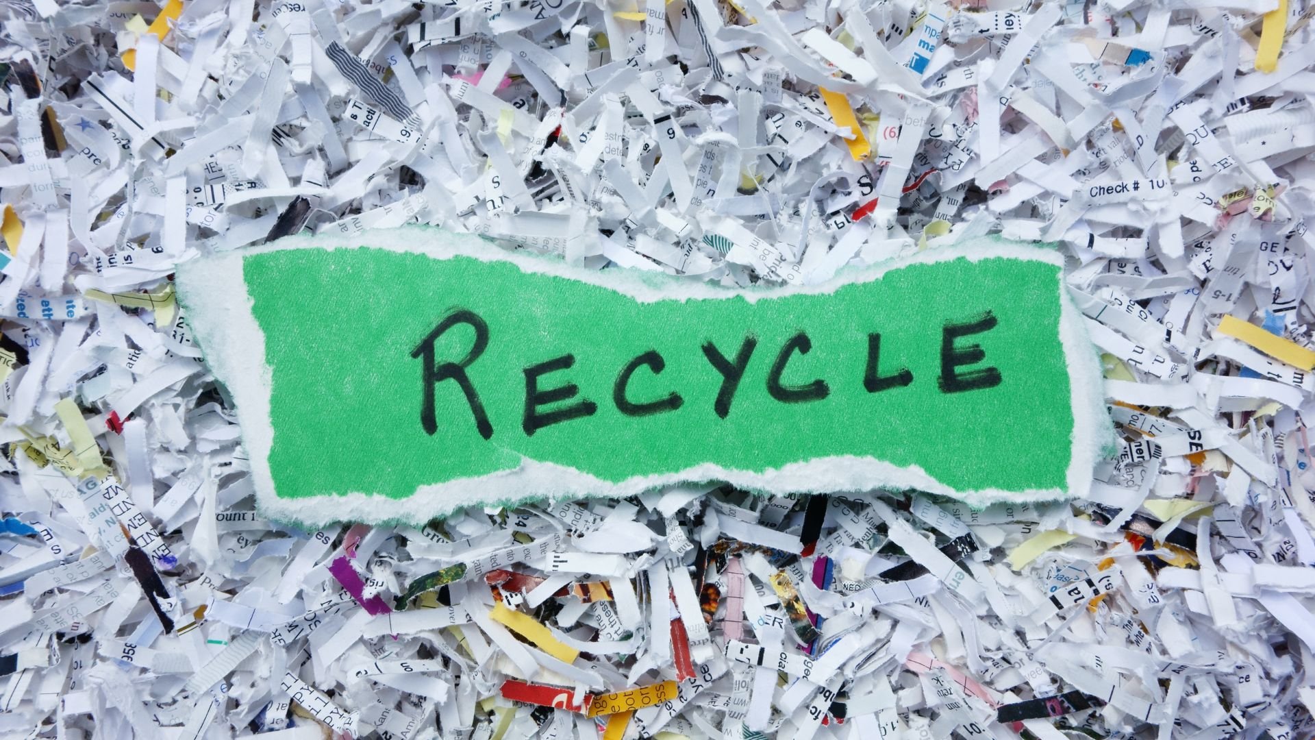 Green recycle sign on scattered shredded paper background